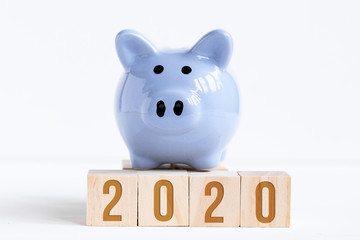 Piggy bank stands on wooden cubes with numbers symbolizing new year 2020.