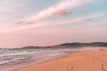 Fototapeta na wymiar Playa idílica y solitaria en otoño con línea de huellas con cielo de hermosas nubes rosadas