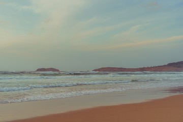 Fototapeta na wymiar Playa idílica y solitaria con olas y un cielo con nubes