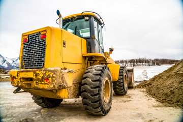 Focus on a yellow bulldozer with snowy mountain and cloudy sky in the background
