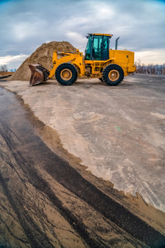 Yellow bulldozer on a road with mound of soil and cloudy sky background