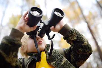 Little boy scout with binoculars during hiking in autumn forest. Child is looking through a...