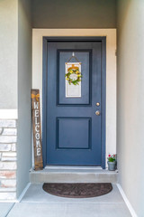Blue front door of a home decorated with wreath welcome sign and potted flower