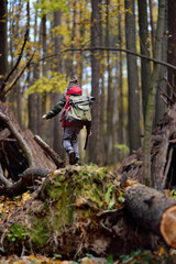 Little boy scout with backpack and rope during hiking in autumn forest. Behind the child is teepee...
