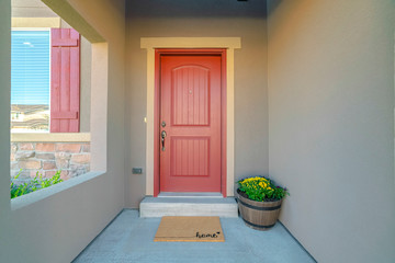 The red front door of a house with concrete exterior wall and shutters on window