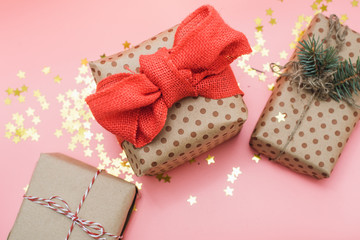 Craft gifts with red bow on pink pastel background with gold confetti. The view from the top, flat lay
