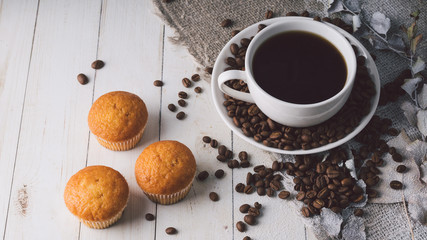 Close up still life, cup of coffee with muffins. Freshly baked delicious muffins and cup of coffee on wooden table. Cup of fresh aromatic coffee and cupcake at table in cafe.