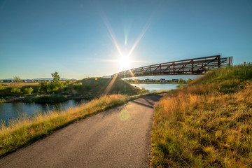 Bridge over paved trail and scenic lake viewed against clear sky and bright sun
