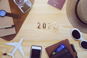 Top view of "2020" text with notebook,traveler accessories,camera,smartphone and airplane on wood table top background with copy space for text.Travel new year holiday vacation concept.