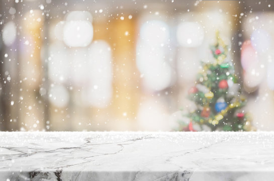 Empty white mable stone table top on blur with bokeh Christmas tree and new's year decoration on window background with snowfall - can be used for display or montage your products.