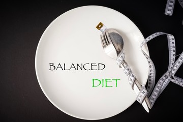 Healthy eating concept. “Balanced Diet” wordings on top of a white plate with fork and spoon and measuring tape. 
