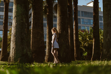 silhouette of a girl among the thick trunks of palm trees on the background of the building