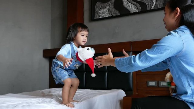 Mother and her daughter playing together in the bedroom. The child having fun and jumping on the bed. Family relaxation time in vacation day.