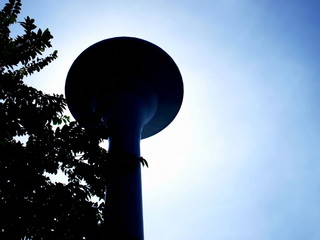 Silhouette water tank tower of metal on the left side of the tree. For the storage and distribution of water in the establishment. On a background of blue sky With space to copy