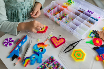 Fototapeta premium Cute little girl makes a toy with thermo mosaic. Development, modeling, education, design with hot plastic. Modern technologies. DIY.