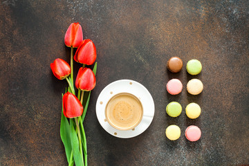 Red tulips, macarons and coffee cup on dark table. Top view with copy space