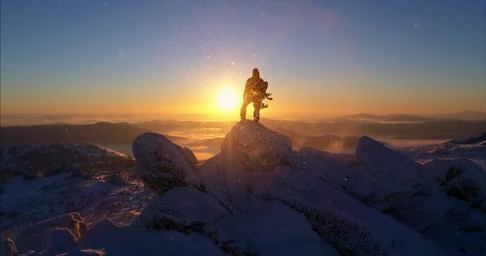 Aerial view. Freerider stands on top of the mountain, snowboard in hand. movable camera plans. Fresh powder. Extreme freeride skiers skiing from the top. beautiful storm of snow flying in the frame