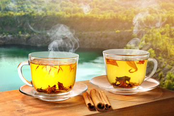 Cups of hot tea with spices on table near lake
