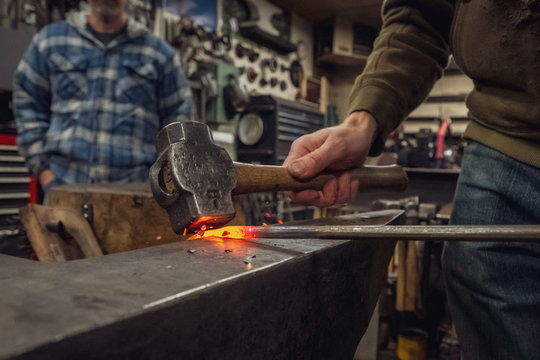 A hammer striking a red hot piece of metal on an avil