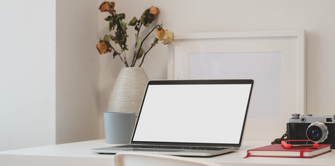 Contemporary workspace with laptop computer, camera, office supplies and dry roses vase