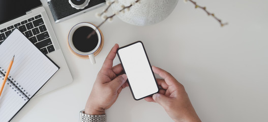 Top view of man holding blank screen smartphone in minimal office room with laptop