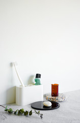 Bathroom amenities in minimal style on white wall background concrete table top. Stylish and modern trendy room interior decoration. Toothbrush, toothpaste, plant, stone, terrazzo, concrete elements.
