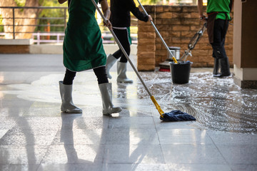 cleaner with mop and uniform cleaning hall floor of public business building