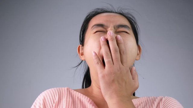 Young Asian woman with yawn expression on grey background.