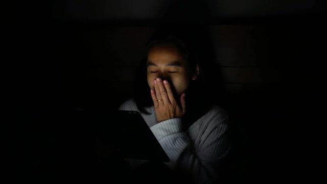 Asian woman yawn and sleepy while using tablet in bedroom at night. Technology and Health care concept.