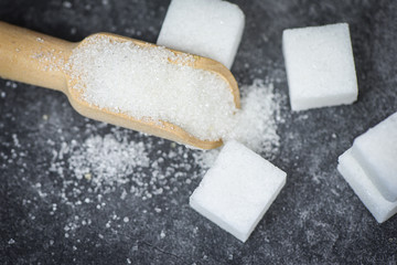 White sugar and sugar cubes on the wooden scoop with dark background