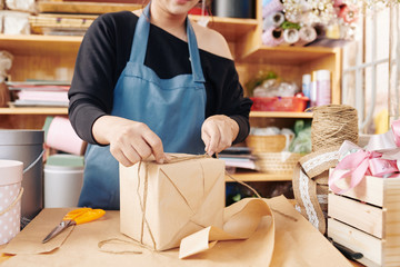 Cropped image of flower shop worker tying wrapped gift box with cord