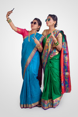 Indian Beautiful young girls in traditional wear, Nauvari saree & sunglasses. Taking selfie pictures on white background.