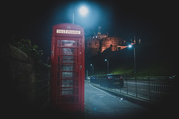 EDINBURGH, SCOTLAND DECEMBER 13, 2018: Old British red phone booth beside the road at night with castle in the background.