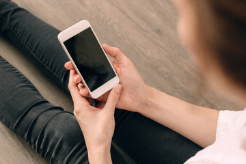 Woman hand holding white mobile phone and sitting on sofa at home.
