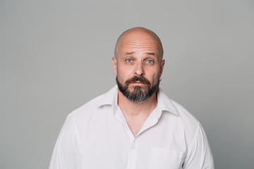 Obraz premium Serious middle-aged man with folded arms and a deadpan expression posing in front of a gray background with copy space
