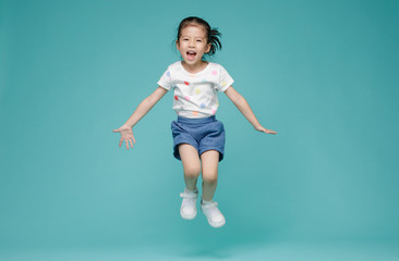 Excited Asian little girl jumping in mid-air, empty space in studio shot isolated on colorful blue background