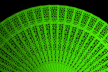 Green colored cardboard fan with an openwork pattern isolated on black closeup