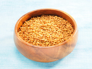 Fenugreek in wooden bowl on a blue background. Indian cuisine, ayurveda, naturopathy, modern apothecary concept