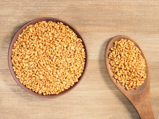 Fenugreek in clay plate and spoon on a brown wooden background. Indian cuisine, ayurveda, naturopathy, modern apothecary concept