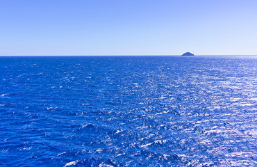 Vivid blue sea and sky  and distant small rock island, sunny summer day.