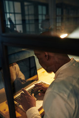 Black businessman working on laptop overtime in dark room all night long to complete project within deadeline