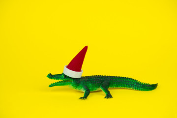 funny green crocodile toy in little santa claus hat  on vibrant yellow background