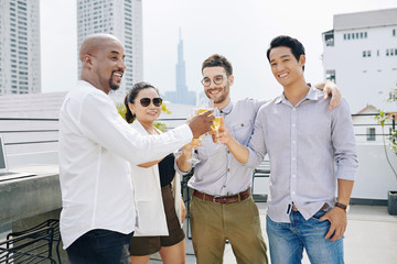Obraz premium Positive multi-ethnic business people clinking glasses of sparkling wine when attending rooftop at party