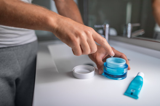 Man Applying Cream Morning Skincare Regimen Moisturizing Face Skin At Bathroom Mirror. Male Beauty Men Skin Care Closeup Of Product Jar And Finger Putting Lotion.