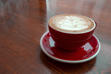 freshly brewed coffee with milk and foam pattern poured into a red ceramic mug on a vintage wooden table in the coffee shop