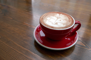freshly brewed coffee with milk and foam pattern poured into a red ceramic mug on a vintage wooden table in the coffee shop