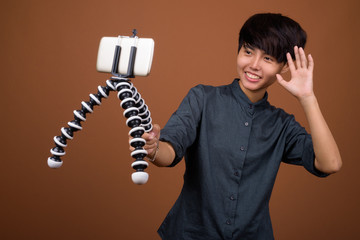 Young beautiful Asian woman with short hair against brown backgr