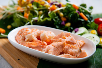 Fresh salad plate with shrimp, salmon, tomato and mixed greens  on wooden background .