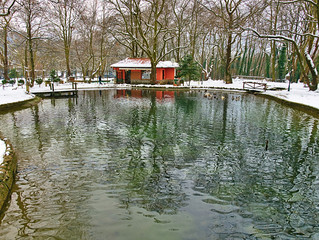 Park pond at winter time, bare trees on snow covered land. Agios Nikolaos (Saint Nicholas) park in Naousa, Greece.