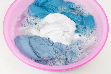 White and blue clothes washed with a basin with soap bubbles, close-up